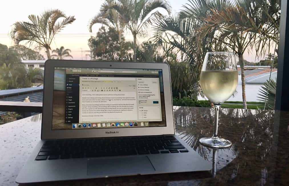 Laptop with a glass of wine and palm trees in the background