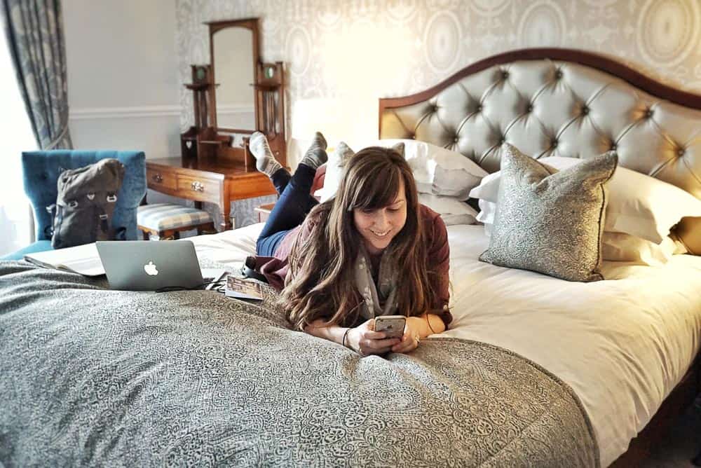 How to Find your Blogging Niche - Lying on hotel bed working on phone with laptop