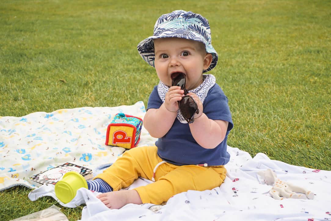 Baby on blanket on grass with toys