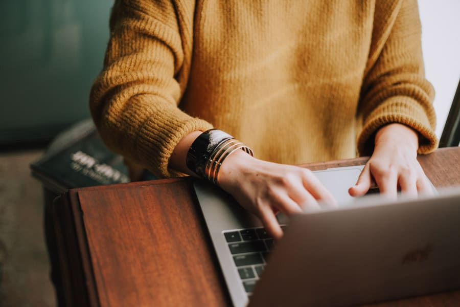 A girl in a yellow sweater is writing on a laptop-How to write an interesting blog post